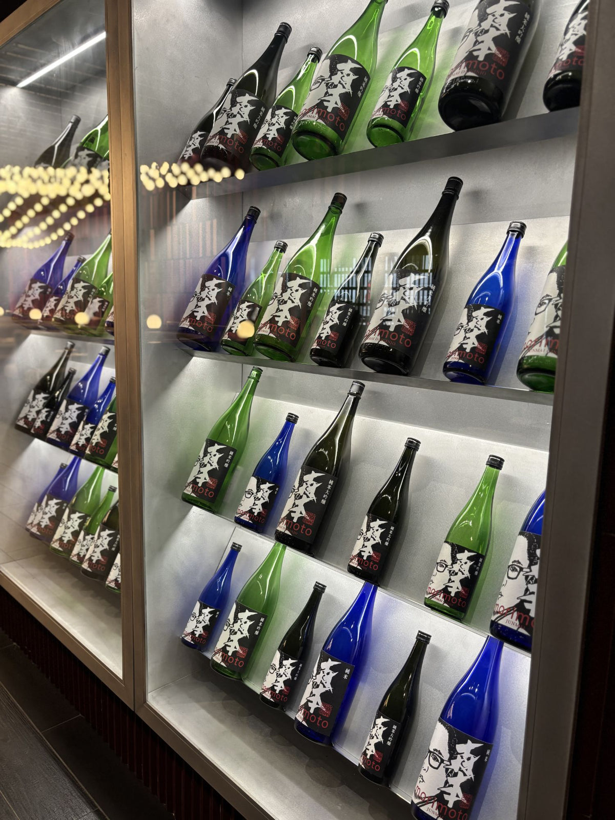 Angled metal shelves holding sake bottles behind glass at MM by Morimoto in Montclair, NJ, built by HM Metalworks