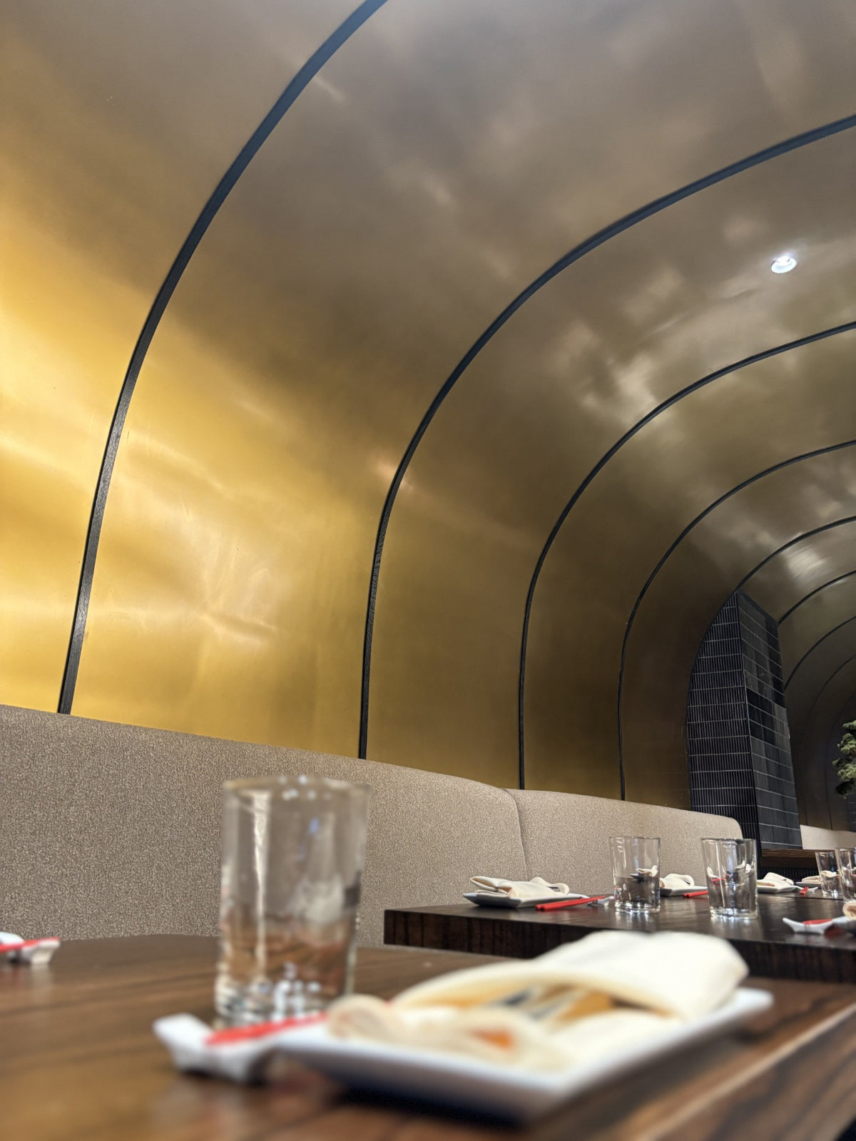 Curved bronze wall panels arching over the banquettes at MM by Morimoto in Montclair, NJ, built by HM Metalworks